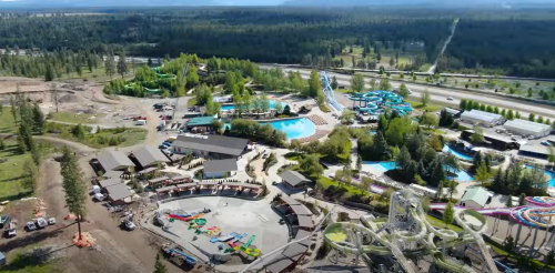 Aerial view of a water park featuring pools, slides, and surrounding greenery, with a highway in the background.